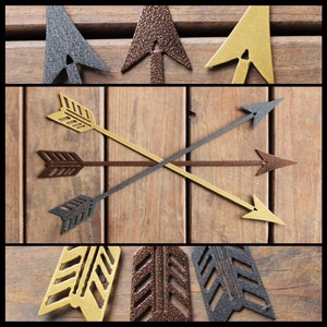 May include: Five decorative metal arrows in a rustic wood background. Two arrows are gold, two are black, and one is brown. The arrows are arranged in a cross pattern.