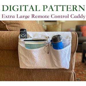 May include: White quilted fabric remote control caddy with three pockets. The caddy is attached to the arm of a brown couch. A remote control, glasses, and a blue water bottle are in the pockets.