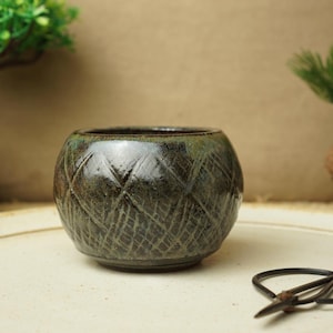 May include: A dark green ceramic planter with a geometric pattern. The planter is sitting on a white surface.