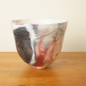 May include: A white ceramic bowl with a wide rim and a flared base. The bowl has a unique abstract design with black, red, and white paint splatters.