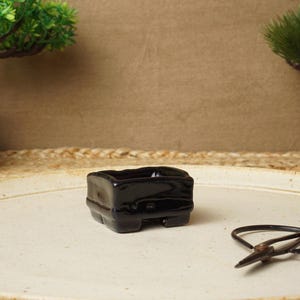 May include: A black ceramic bonsai pot with a square shape and a glossy finish. The pot is sitting on a white ceramic tray.