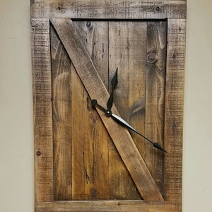 May include: A rectangular wooden wall clock with a rustic, farmhouse aesthetic. The clock face is made of vertical wooden planks with a diagonal wooden accent. Black clock hands indicate the time. The frame is made of weathered wood.