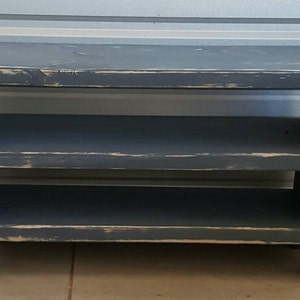 K&ouml;nnte beinhalten: Ein dunkelblaues Holzregal mit zwei Ablagen. Das Regal hat eine rechteckige Oberseite und eine Used-Optik mit sichtbaren Gebrauchsspuren, was ihm ein rustikales Aussehen verleiht. Das Regal ist f&uuml;r die Aufbewahrung und Pr&auml;sentation konzipiert und ist 76 cm breit.