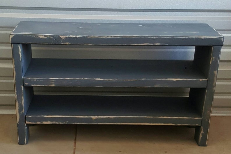 K&ouml;nnte beinhalten: Ein dunkelblaues Holzregal mit zwei Ablagen. Das Regal hat eine rechteckige Oberseite und eine Used-Optik mit sichtbaren Gebrauchsspuren, was ihm ein rustikales Aussehen verleiht. Das Regal ist f&uuml;r die Aufbewahrung und Pr&auml;sentation konzipiert und ist 76 cm breit.