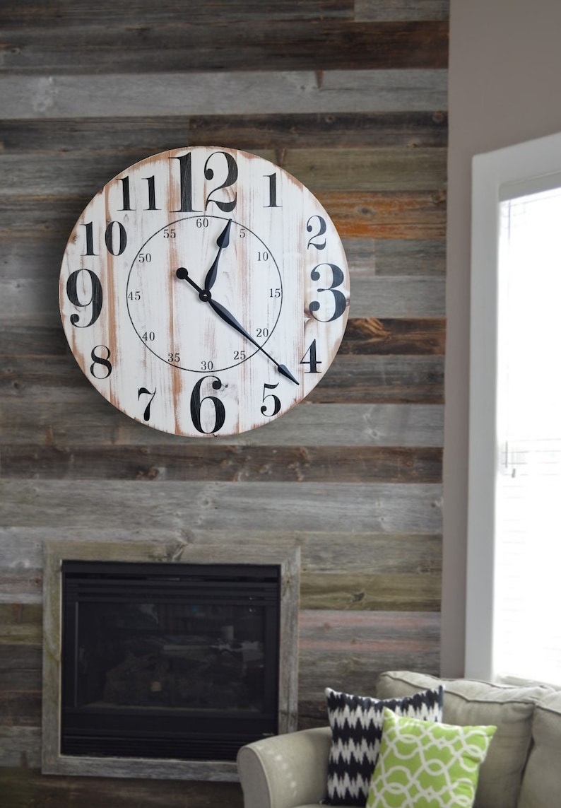 K&ouml;nnte beinhalten: Eine wei&szlig;e Uhr im Landhausstil mit schwarzen r&ouml;mischen Ziffern und schwarzen Zeigern. Die Uhr h&auml;ngt an einer Wand mit wiederverwendeten Holzdielen.