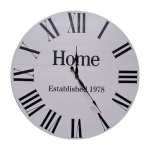 May include: A round, white wall clock with black Roman numerals and hands. The word "Home" is printed in black, along with "Established 1978". The clock face has a distressed, wooden plank design, adding a rustic touch to the decor.