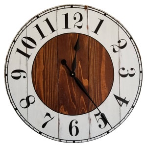 May include: A white and brown wooden clock with black Roman numeral hour markers and black hands. The clock face has a distressed white finish and the numbers are painted in black. The clock has a brown wooden center with a wood grain pattern.