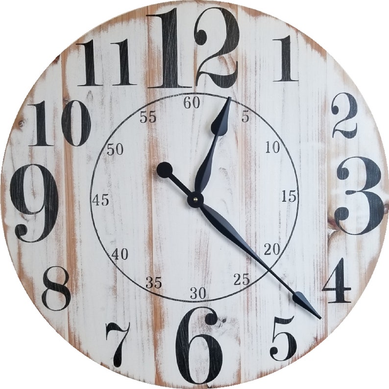K&ouml;nnte beinhalten: Eine wei&szlig;e Holzuhr mit schwarzen r&ouml;mischen Ziffern als Stundenmarkierungen und schwarzen Zeigern. Das Zifferblatt der Uhr hat einen abgenutzten Look mit sichtbarer Holzmaserung. Das Zifferblatt der Uhr hat auch schwarze Markierungen f&uuml;r die Minuten.