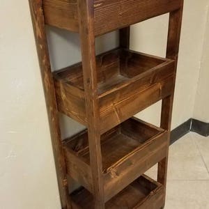 May include: A wooden storage shelf with four open bins. The shelf is stained a dark brown color, with visible wood grain. The design is a simple, rustic style, suitable for various storage needs.