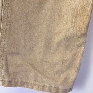 May include: Close-up of tan-colored canvas fabric, showing the texture and stitching details. The fabric has some minor discoloration and wear, suggesting it is a well-used item. The bottom hem is visible.