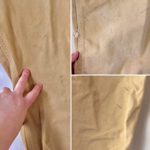 May include: Close-up of tan-colored work pants, showing details of the fabric and stitching. The image highlights the texture and color variations of the pants, with some visible wear and tear.