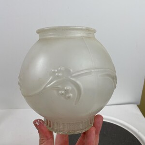 May include: Frosted glass light fixture globe with a round shape and a decorative floral design. The globe has a clear, ribbed base and a smooth, rounded top. The overall color is a soft, opaque white.