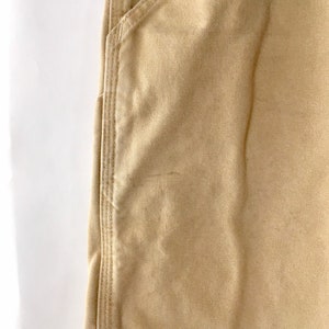 May include: Close-up of tan-colored work pants. The image shows a pocket and the seam detailing on the pants. The fabric has a textured appearance. The pants are made of a durable material.