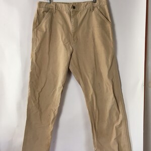 May include: Tan work pants with a button closure, front pockets, and a straight leg. The pants are hanging on a clear hanger against a white background. The pants appear to be made of a durable fabric.