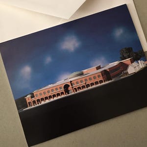 May include: A greeting card featuring a detailed architectural rendering of a building with a red brick facade, arched windows, and a domed roof. The card is set against a backdrop of a blue sky with scattered clouds, and is accompanied by a white envelope.