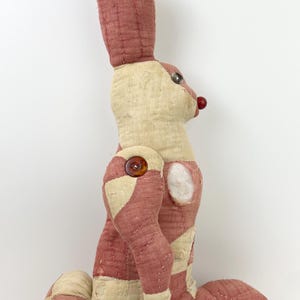 May include: A vintage stuffed rabbit toy in a patchwork design. The rabbit features a cream and red color scheme, with button and bead accents for the eyes and nose. The toy has long ears and is in a seated position.