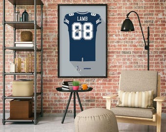Può includere: Opera d'arte incorniciata con una maglia da football blu navy con il nome "LAMB" e il numero "88" in bianco. Il design della maglia include dettagli bianchi e argento su uno sfondo grigio. La parola "Cowboys" è in basso.