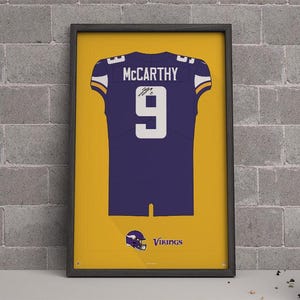 May include: Framed print of a purple and gold football jersey with the name "McCarthy" and the number "9". The jersey is set against a yellow background with the team's logo and the word "Vikings".