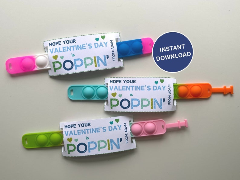 May include: A collection of colorful pop-it fidget toys with Valentine's Day cards. The cards read "Hope Your Valentine's Day is Poppin'" and include the text "From: Adam". The toys are pink, blue, green, and orange.