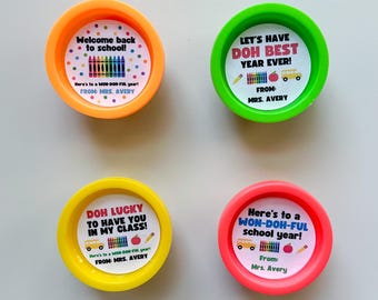 May include: Four colorful, circular containers with lids. Each lid has a different message in a playful font, such as "Welcome back to school!" and "Doh Lucky to have you in my class!" The containers are orange, green, yellow, and red.