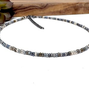 May include: A delicate silver and gray beaded choker necklace with a silver clasp.