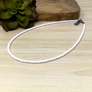 Pode incluir: Um colar choker de contas brancas com um fecho prateado.