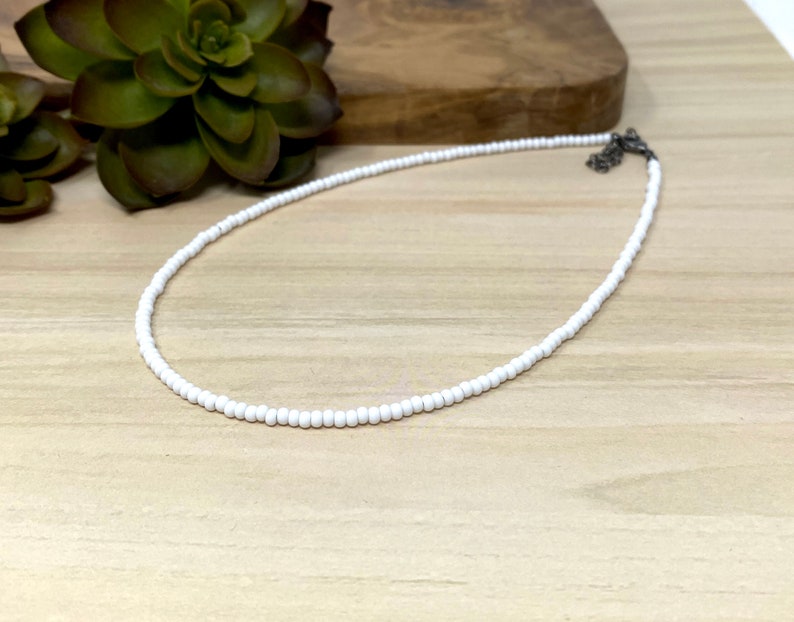 Pode incluir: Um colar choker de contas brancas com um fecho prateado.