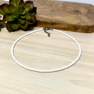 Pode incluir: Um colar choker de contas brancas com um fecho prateado.