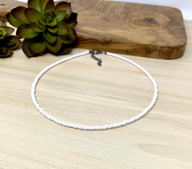 Pode incluir: Um colar choker de contas brancas com um fecho prateado.