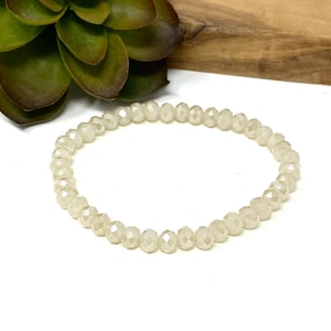 May include: A white beaded bracelet made of small, faceted beads. The bracelet is simple and elegant, and would make a great gift.