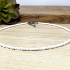 Pode incluir: Um colar choker de contas brancas sobre uma superf&iacute;cie de madeira clara.