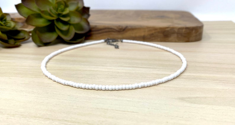 Pode incluir: Um colar choker de contas brancas sobre uma superf&iacute;cie de madeira clara.