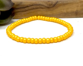 May include: A simple gold beaded bracelet. The bracelet is made of small, round beads that are strung together on a thin cord.