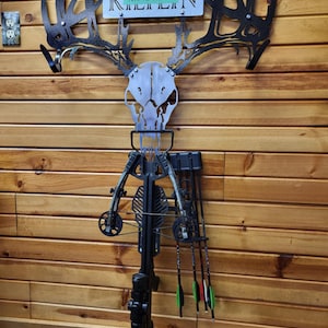 May include: A black metal deer skull wall mount with antlers, a crossbow, and arrows. The metal plate above the skull reads "NAME HERE".