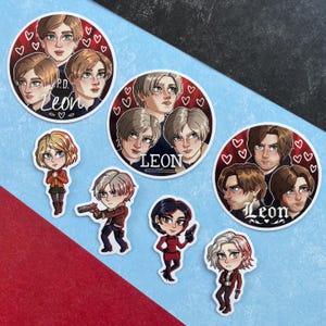 May include: A selection of vibrant stickers showcasing anime-style character illustrations. The stickers include circular designs with multiple character portraits and the name "Leon", alongside individual character designs. The background is a mix of blue and red.