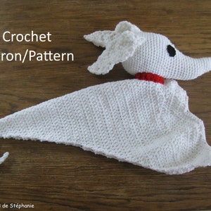 Pode incluir: Amigurumi fantasma branco de crochê com nariz vermelho e olho preto. O fantasma está deitado sobre uma superfície de madeira. Padrão de crochê/padrão.