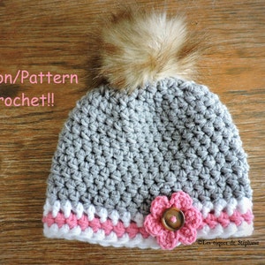 May include: Grey crocheted hat with a white and pink trim, a pink flower with a brown button in the centre, and a brown faux fur pom pom on top. The hat is labelled "Patron/Pattern Crochet!"