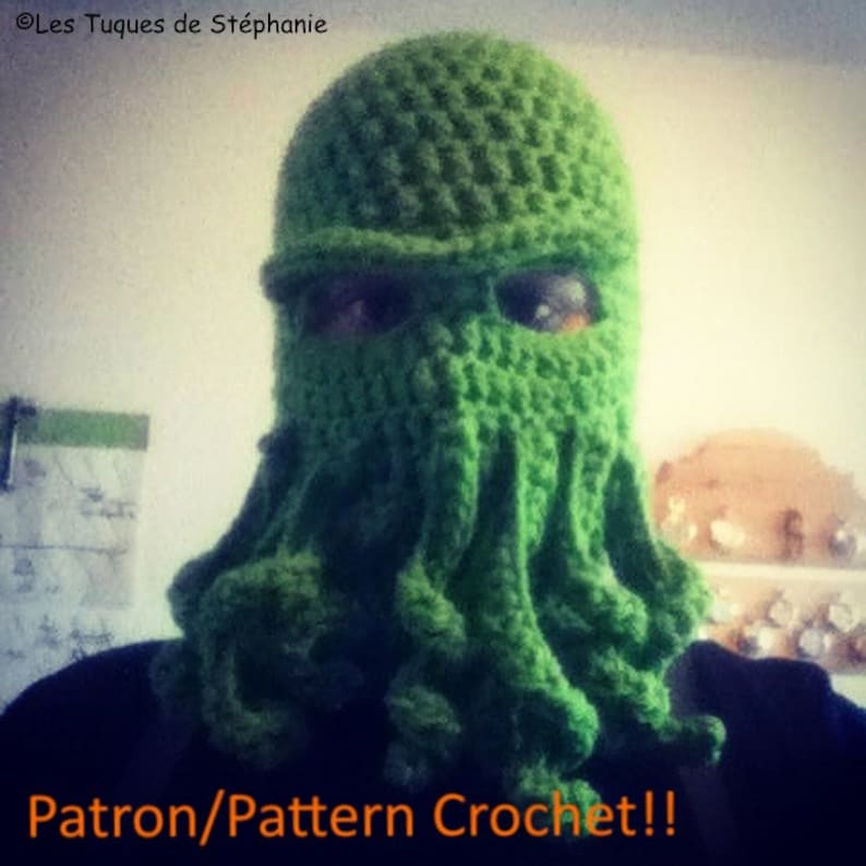 May include: Green crocheted hat with a long, tentacle-like design. The hat covers the entire head and face, with only the eyes visible. The text "Patron/Pattern Crochet!!" is written in orange at the bottom of the image.