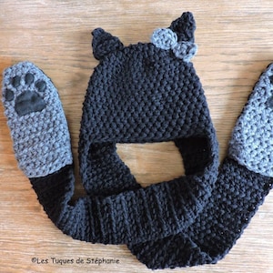 May include: Black and gray crocheted hat with ear flaps and paw print mittens attached to a matching scarf. The hat has a black bow on top.