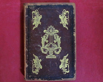 May include: A brown leather-bound book with gold-leaf embellishments. The cover features a decorative design with two cherubs flanking a lyre.
