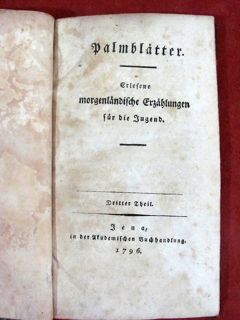 May include: A vintage book titled "Palmblätter. Erlesene morgenländische Erzählungen für die Jugend."  The book is open to the title page and shows the text "Dritter Theil. Jena, in der Akademischen Buchhandlung. 1796."