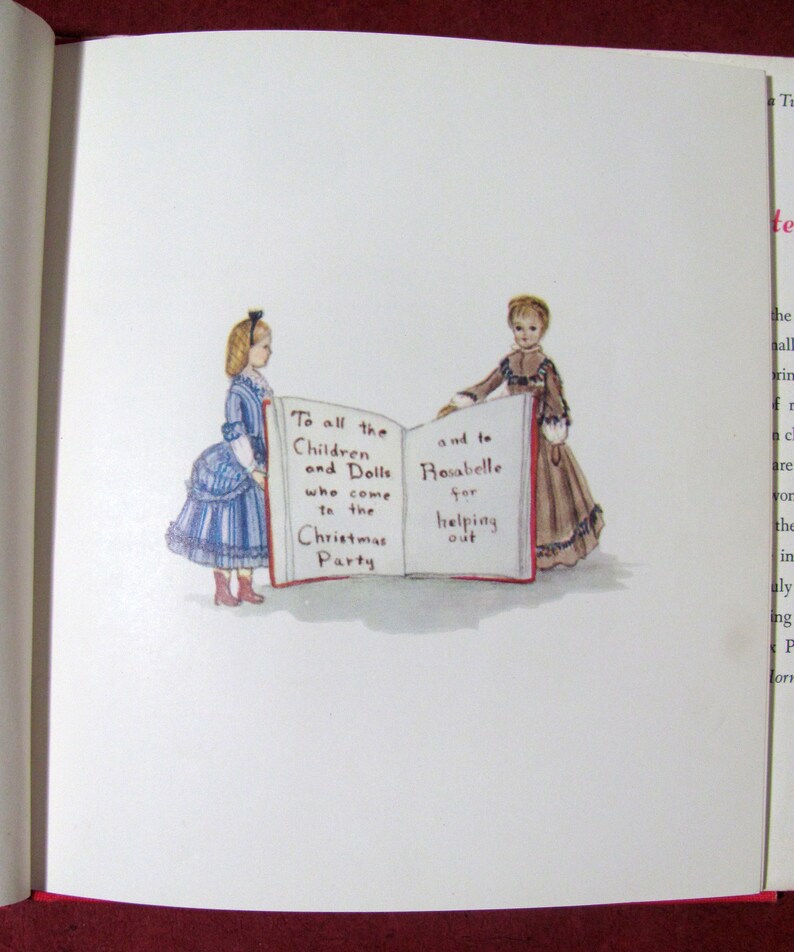 May include: Two dolls, one in a blue and white dress and the other in a brown dress, stand on either side of an open book. The book is open to a page with the text "To all the Children and Dolls who come to the Christmas Party" on the left side and "and to Rosabelle for helping out" on the right side.