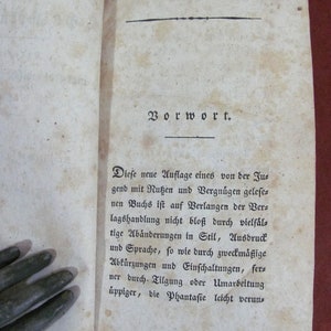 May include: An open antique book page with aged, off-white paper featuring dark brown foxing spots. The text is printed in a black Fraktur typeface, beginning with the heading Vorwort, followed by a paragraph of German text starting with Diese neue Auflage.