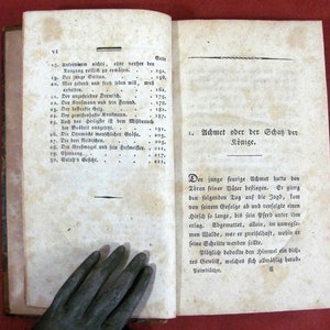 May include: An open antique book with aged, off-white paper pages featuring black printed German text. The left page displays a numbered table of contents, while the right page shows a chapter title, Achmet oder der Schatz der K&ouml;nige, and text.