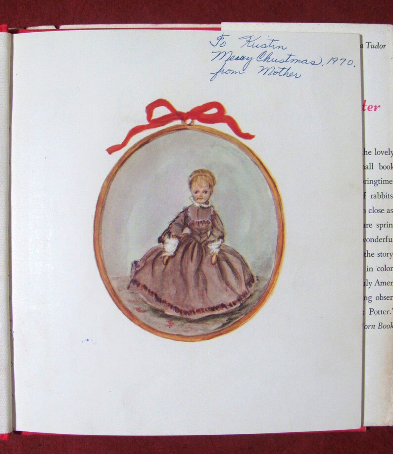 May include: A vintage illustration of a young girl wearing a brown dress and a white lace collar. The illustration is framed in a gold oval and surrounded by a red ribbon. The text "To Kustin Merry Christmas, 1970. From Mother" is written in blue ink on the page.