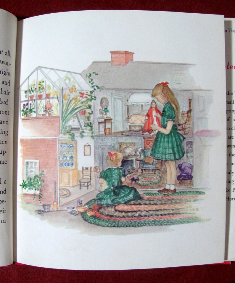 May include: Two girls play in a dollhouse with a green rug, a fireplace, and a doll bed. The dollhouse has a greenhouse on the roof.