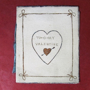 May include: A vintage Valentine's Day card with a cream-colored cover. The card features a heart with the words "TO MY VALENTINE" and a brown heart pierced by an arrow. The card is framed with brown lines and bows.