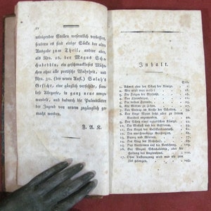 Op de afbeelding: Een open antiek boek met verouderde, gebroken witte papieren pagina's met zwarte gedrukte Duitse tekst. De linkerpagina toont een alinea die eindigt met de initialen F. A. K., terwijl de rechterpagina een inhoudsopgave bevat met de titel Inhalt.
