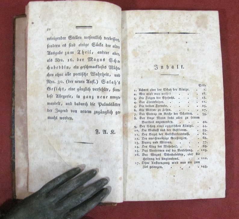 Op de afbeelding: Een open antiek boek met verouderde, gebroken witte papieren pagina's met zwarte gedrukte Duitse tekst. De linkerpagina toont een alinea die eindigt met de initialen F. A. K., terwijl de rechterpagina een inhoudsopgave bevat met de titel Inhalt.