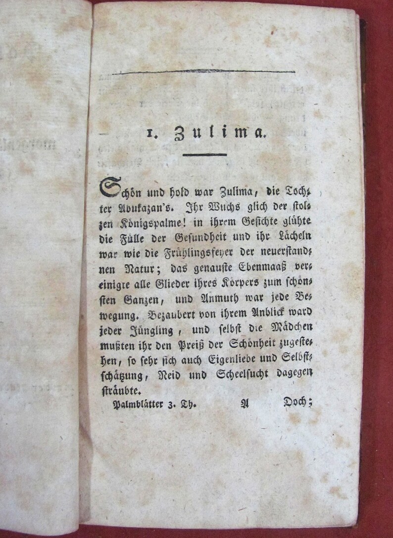 Op de afbeelding: Een open antieke boekpagina met verouderd, gebroken wit papier met zwarte gedrukte Duitse tekst. De koptekst luidt 1. Zulima. De tekst beschrijft een personage genaamd Zulima, met de voettekst Palmbl&auml;tter 3. Th. Het papier vertoont zichtbare vlekken.